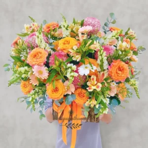 Một người đang ôm giỏ hoa cắm sẵn màu cam – trắng rực rỡ, đại diện cho sản phẩm hoa cắm sẵn gần đây tại Hoa Gửi Yêu Thương.